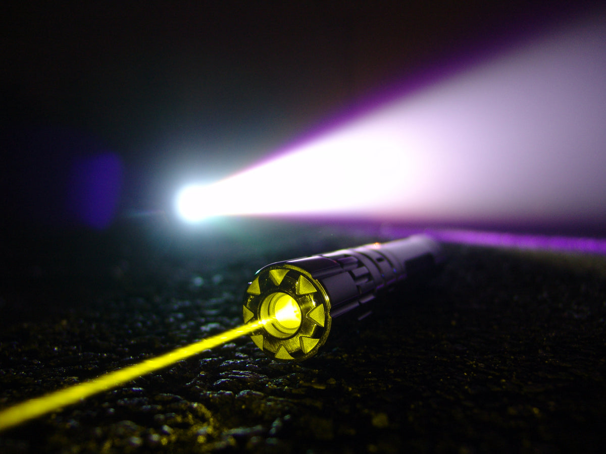 Valkyrie 573nm True Yellow laser on the ground at night, its yellow beam crossing a flashlight beam